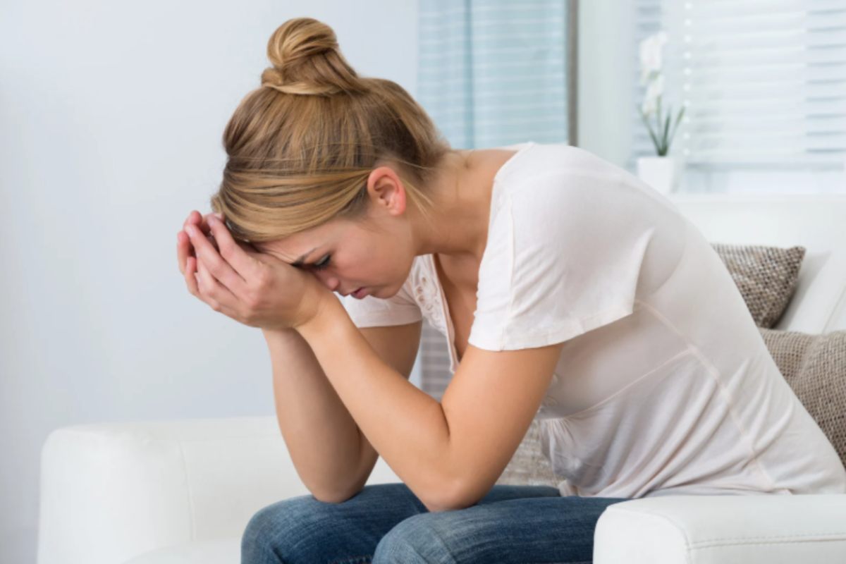 donna stressata seduta sul divano con le mani in fronte